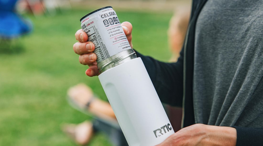 Close-up of a person putting a can inside of a white RTIC Ultimate Skinny Can Cooler.