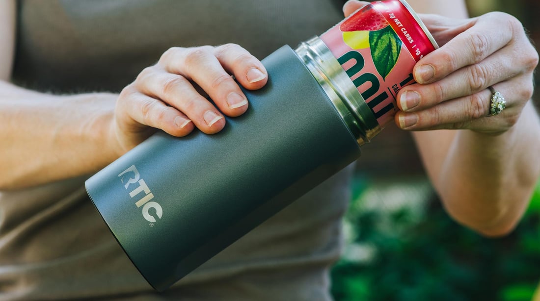 Close-up of a person putting a can inside of a green RTIC Ultimate Craft Can Cooler.