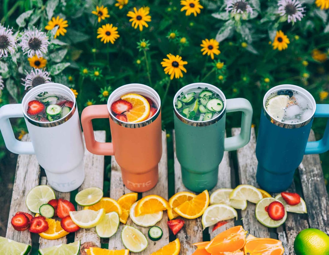 4 different colored RTIC Road Trip Tumblers filled with fruity drinks on a wood table