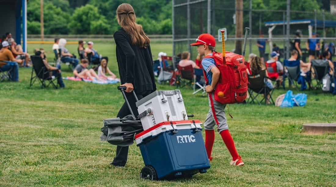 Mom and son pulling RTIC 42 QT Ultra-Light Wheeled Cooler with Halftime Cooler stacked on top to the little league baseball game.