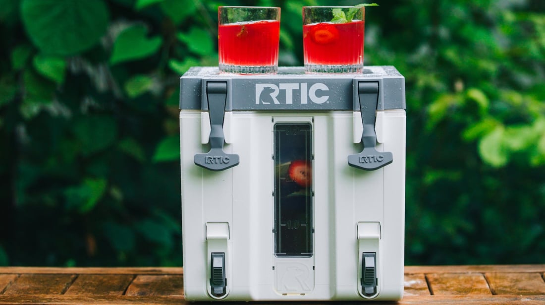 A red punch in two glasses sitting on top of a white RTIC Halftime Cooler on a table.