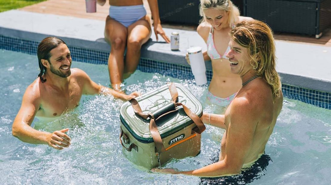 Tan RTIC Soft Pack Cooler floating in a pool with people around