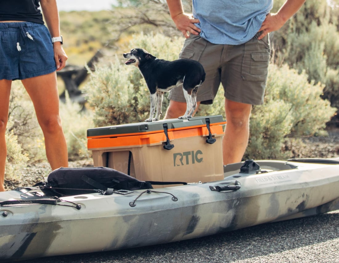 Dog standing on top of a tan RTIC 32QT Ultra-Light Cooler sitting in a kayak