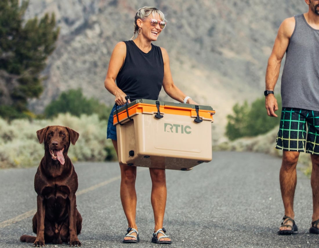 Woman carrying RTIC 32QT Ultra-Light Cooler with her dog sitting next to her