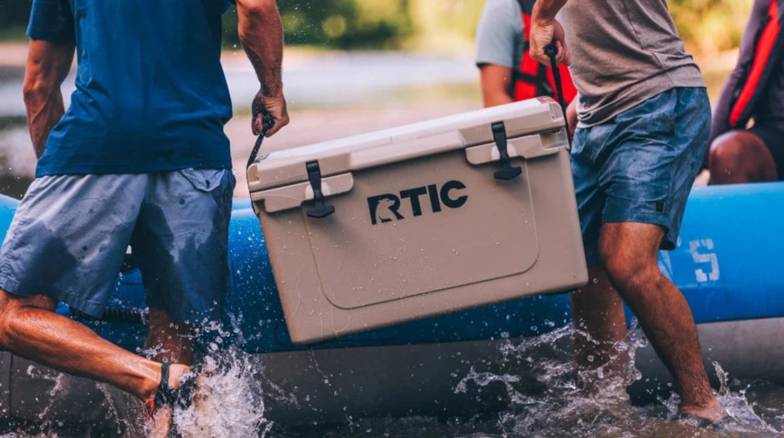 Two men carry a tan RTIC 45QT Ultra-Tough Cooler through water