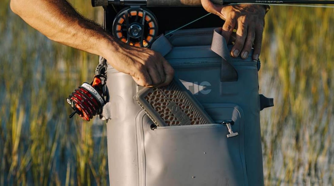 Man fishing in the water reaches into the front pocket of a gray RTIC Ultra-Tough Soft Cooler Pro.
