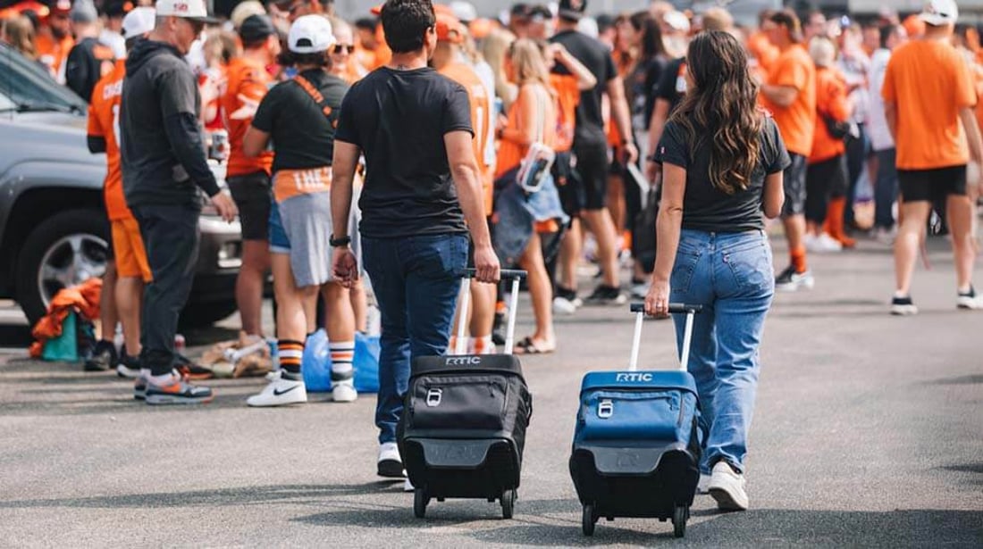 Man and woman roll their RTIC everyday wheeled coolers at a sporting event