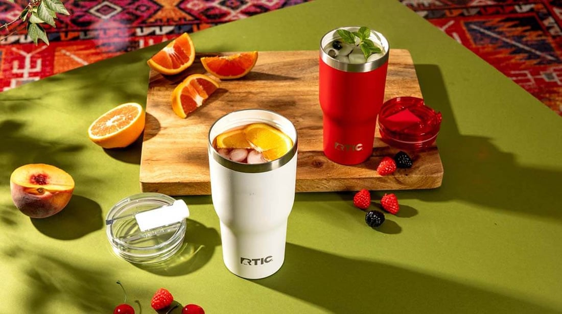 red and white RTIC Essential Tumblers filled with fruit drinks on a green table surrounded by fresh fruit.