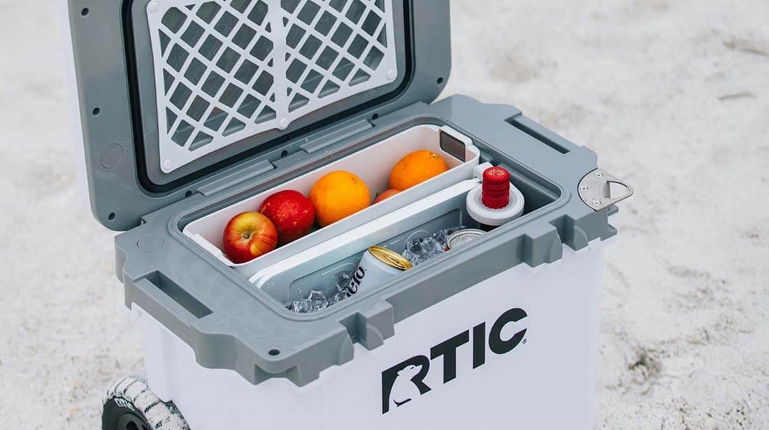 White RTIC 22QT Ultra-Light wheeled cooler packed with ice, drinks, and fruit in the dry goods basket.