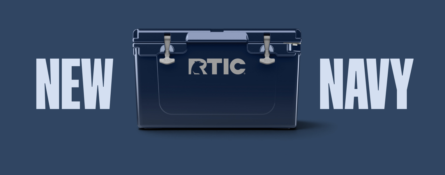 A navy blue RTIC hard cooler in front of the words: New in Navy