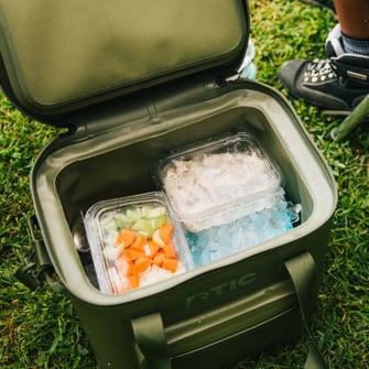 A green RTIC waterproof cooler with ice and food inside.