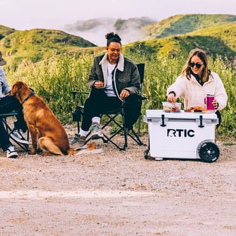 A group o f friends camping with a white RTIC wheeled cooler.