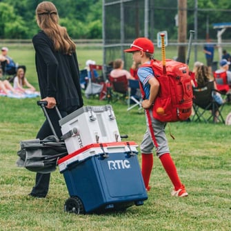 A family pulling a white RTIC wheeled cooler to the baseball field.