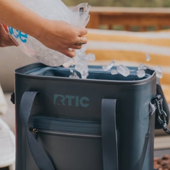 Pouring ice into a navy RTIC waterproof soft cooler.