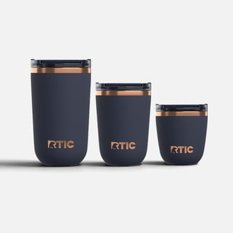 Three dark blue RTIC tumblers with copper trim, arranged from tallest to shortest against a plain white background.