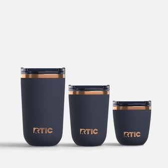 Three dark blue RTIC tumblers with copper trim, arranged from tallest to shortest against a plain white background.