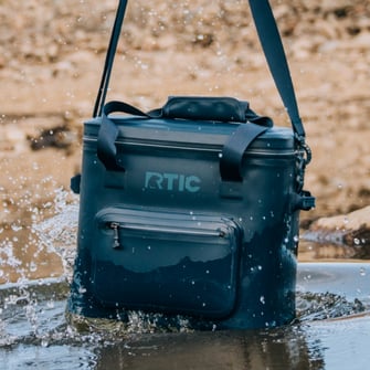 A navy RTIC waterproof soft cooler splashing in water.