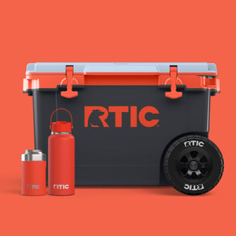 Orange RTIC drinkware and a dark grey hard cooler with orange accents on an orange background.