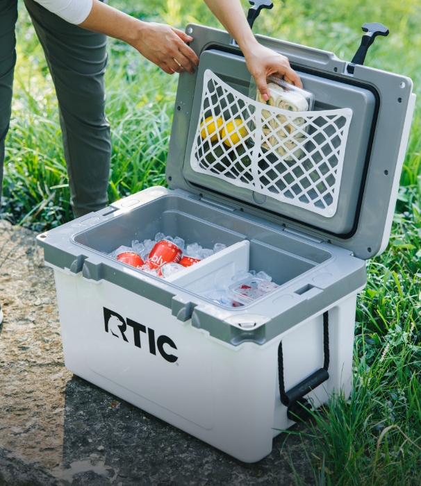 A person putting food into a white RTIC Hard Cooler filled with food and ice.