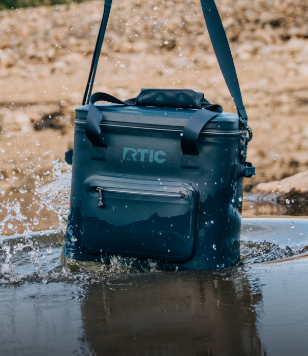 Navy blue RTIC waterproof soft cooler in splashing in water.