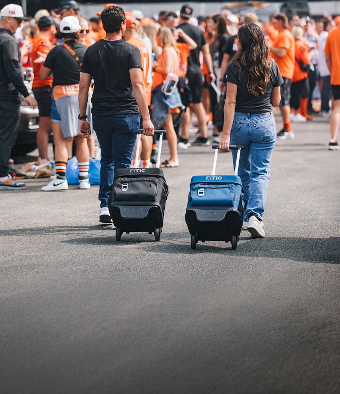 A man and woman pull everyday wheeled RTIC coolers through a crowd wearing orange and black clothing.