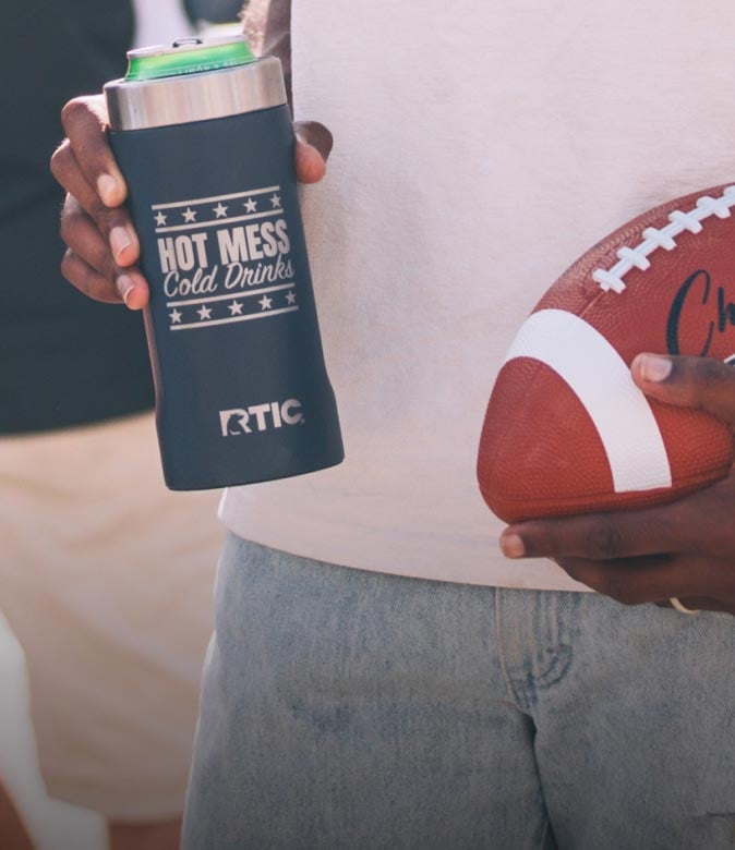Person holding a black RTIC can cooler and football outdoors.