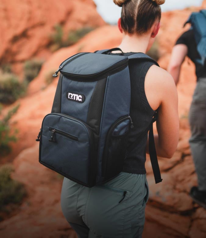 Hiker wearing an RTIC backpack cooler while walking through a red rock canyon.