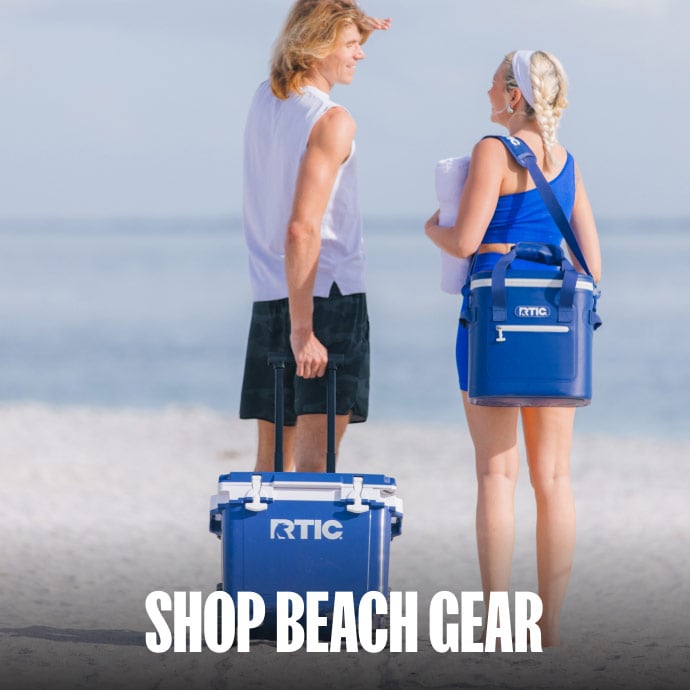 Couple at the beach with blue RTIC hard and soft coolers.