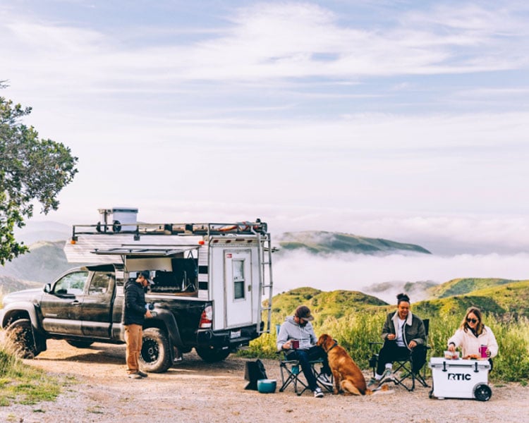 A group of friends car camping on a coastal bluff with an RTIC wheeled cooler.