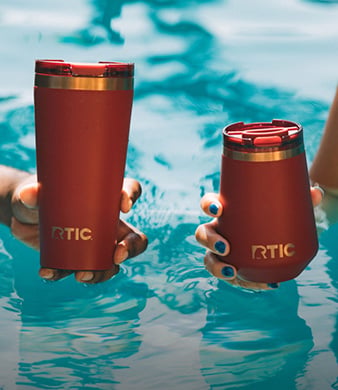 Two red RTIC insulated tumblers held in a swimming pool.
