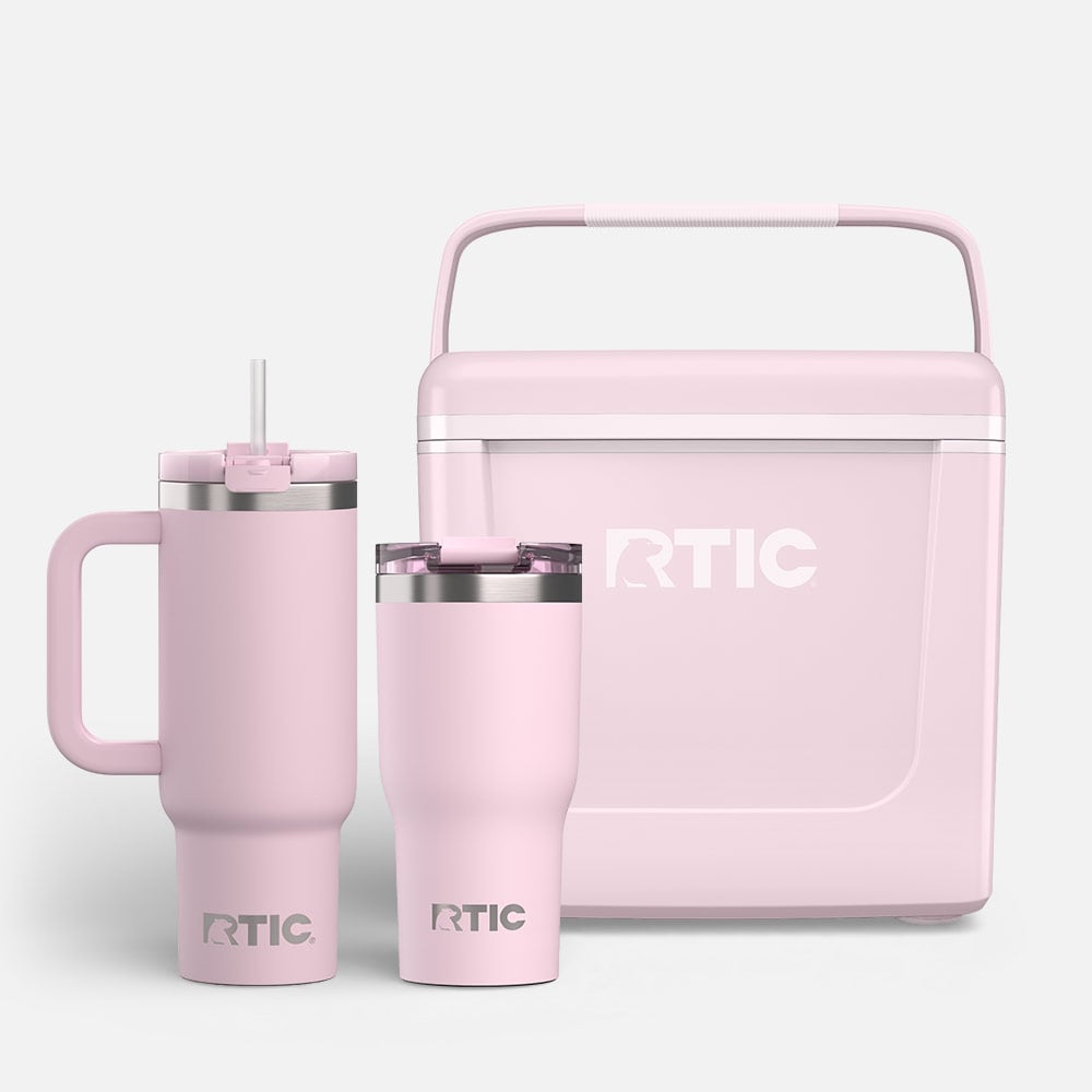 Pale pink RTIC cooler with handle, alongside two insulated tumblers, one with a handle and straw, one without, on a white background.