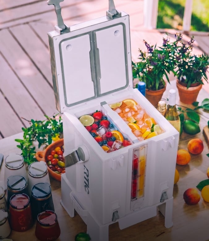 White insulated cooler with fruit-filled drinks and ice on a patio, surrounded by reusable bottles and fresh produce.