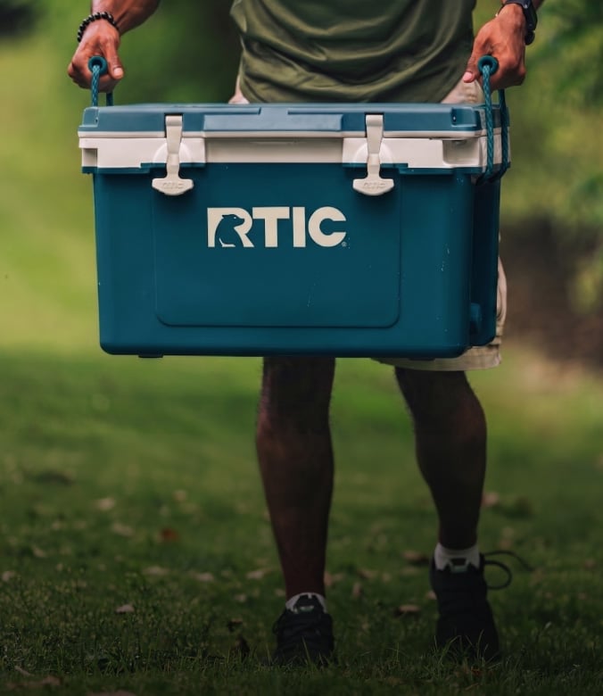 Person walking outside, carrying a marine blue RTIC Ultra-Light Cooler.