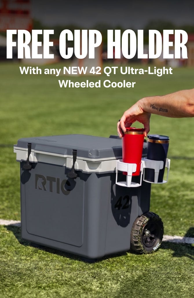 An RTIC 42 QT gray wheeled cooler on grass with a dual cup holder attachment holding two tumblers.