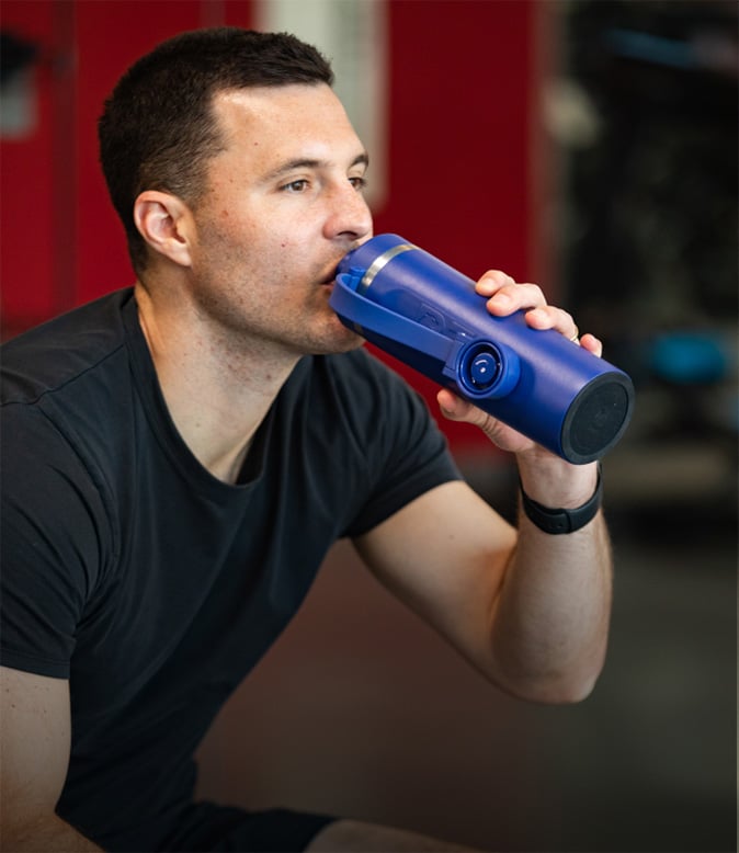 Person drinking from a blue insulated RTIC water bottle in a gym, highlighting hydration and durable drinkware for workouts.