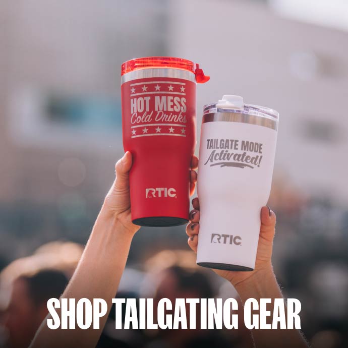 RTIC tumblers and a wheeled cooler used for tailgating at a youth baseball game, with families gathered in the background.