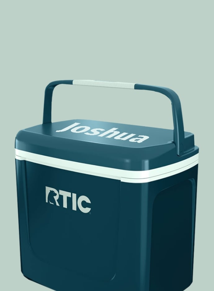 A small dark teal colored RTIC hard cooler with the name Joshua printed on it in a light mint blue - on a seafoam background.