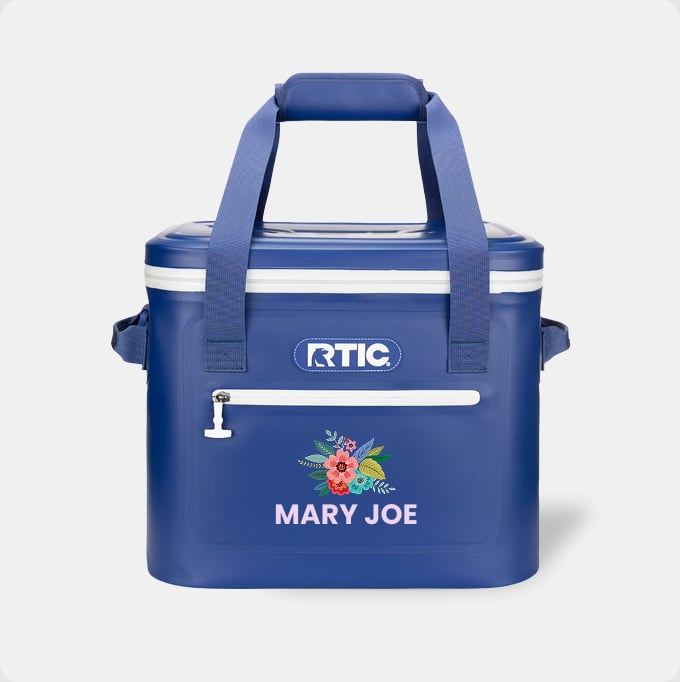 A blue RTIC soft cooler with the name Mary Joe and a flower design on it on a light grey background.