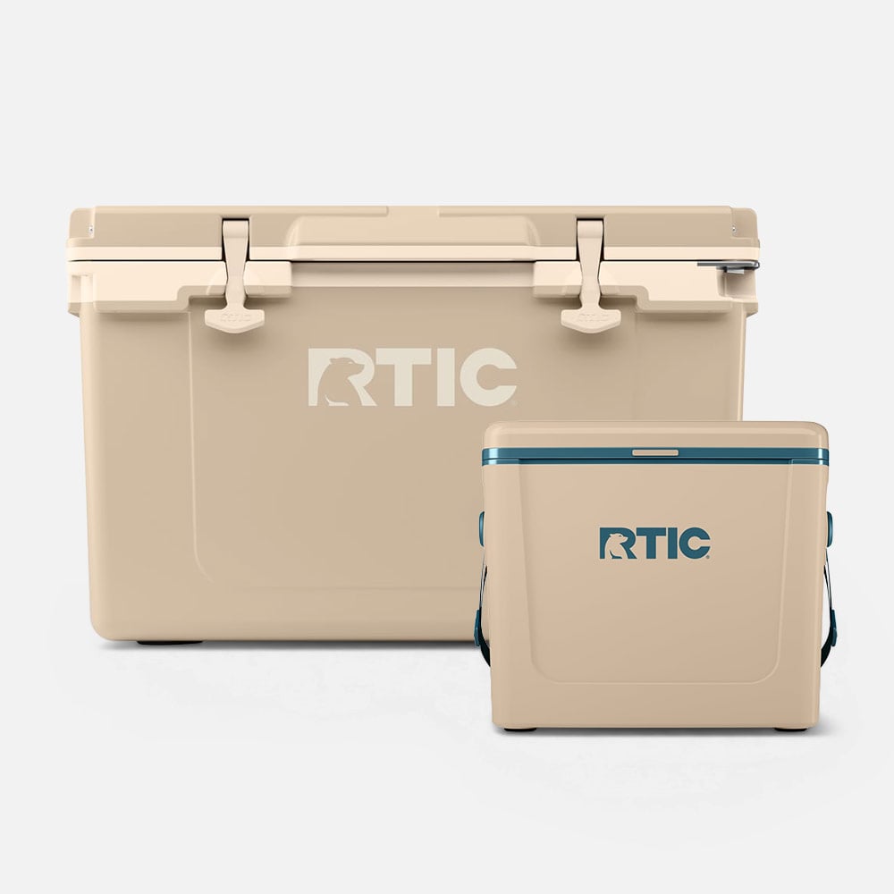Tan RTIC hard cooler with latches beside a smaller matching cooler on a light background.