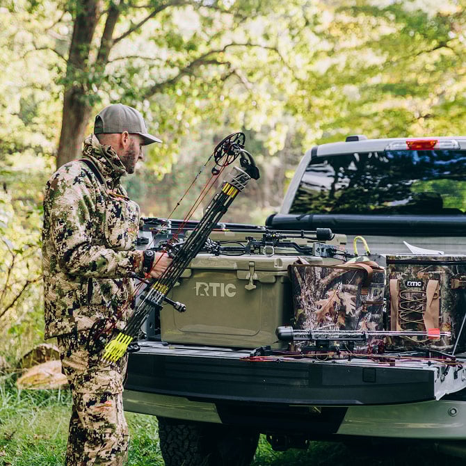 Hunter dressed in camo, standing next to pickup truck.