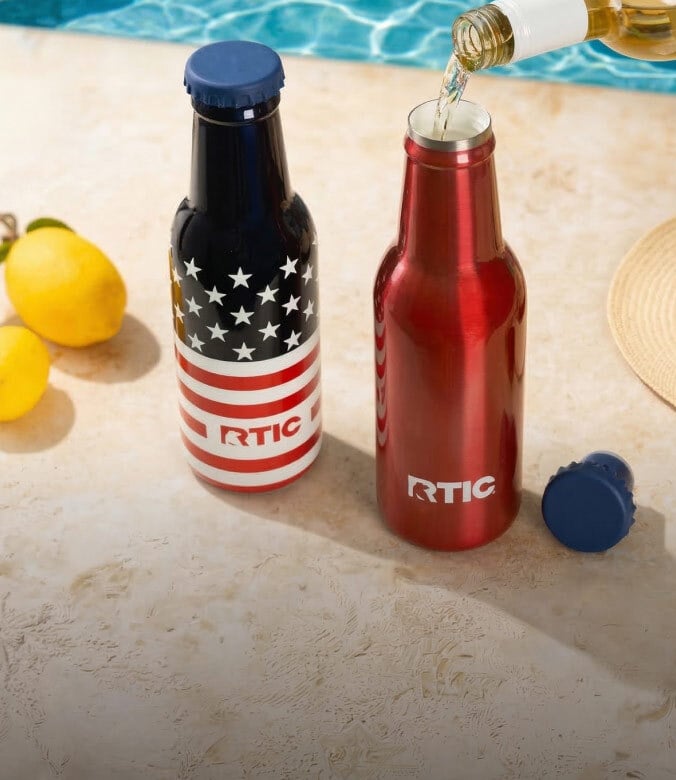 Wine poured into a red RTIC insulated bottle beside an American flag design bottle, lemons, and a poolside setting.