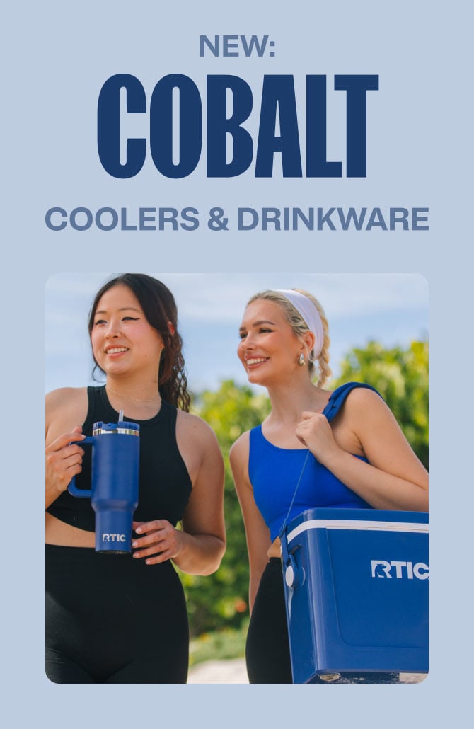 Two women in workout attire smile as they walk outdoors, carrying a blue RTIC tumbler and cooler on a sunny day.