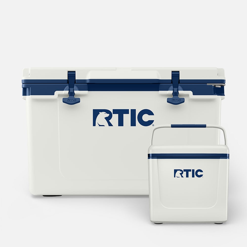 Cool Grey RTIC hard cooler with navy accents beside a smaller matching personal cooler, both shown closed on a clean white background.