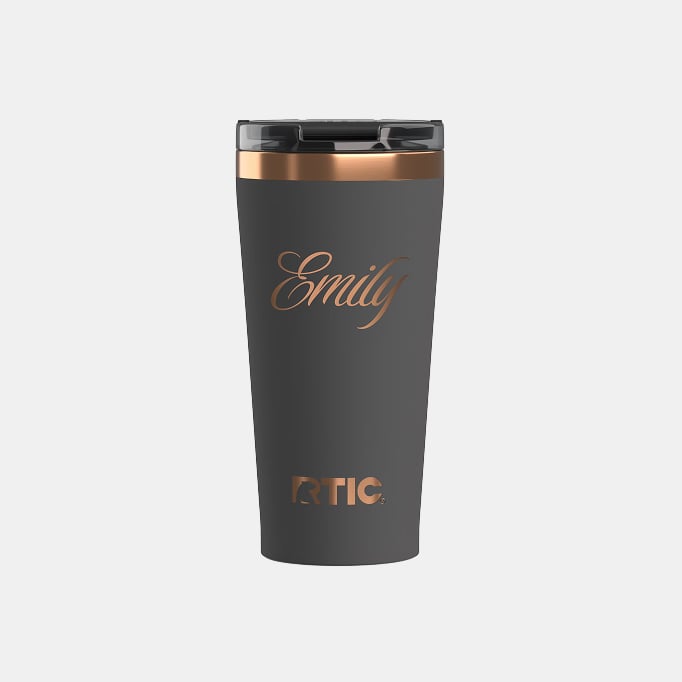 A light black RTIC Happy Hour Pint Tumbler with the name Emily engraved on it on a light grey background.