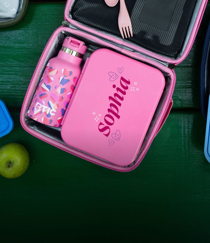 Open pink insulated lunch bag with a personalized pink lunch container, matching RTIC water bottle, reusable utensils, and a green apple.