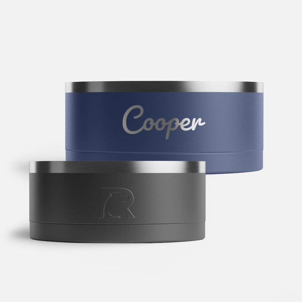Two RTIC dog bowls, one navy personalized with the name Cooper and the other black.