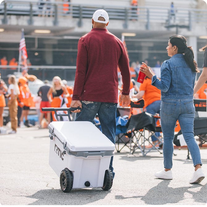 Couple walking through a tailgate with their 52 Ultra-Light Wheeled Cooler.