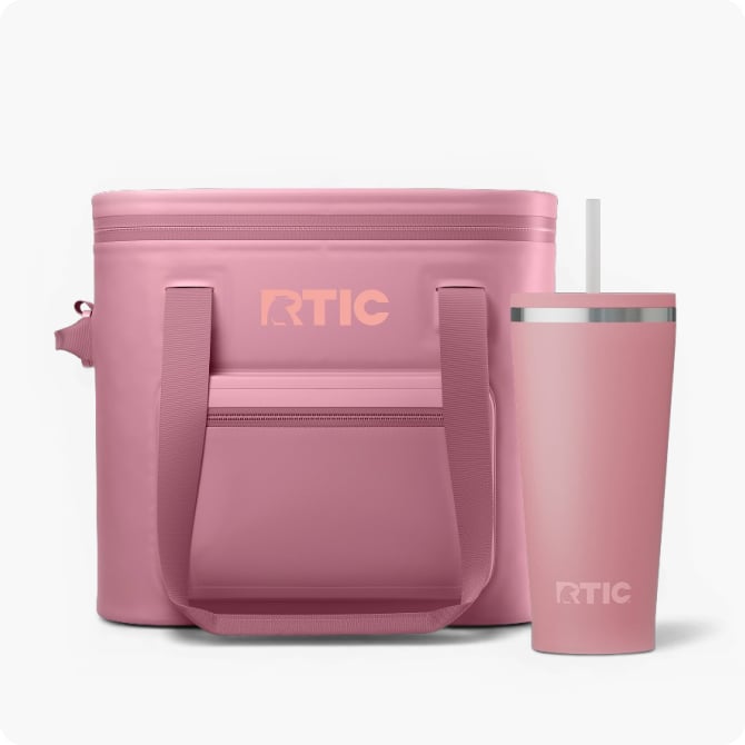 Pink RTIC soft cooler with front pocket and matching insulated tumbler with straw on a clean white background.