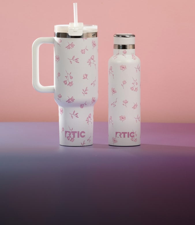 RTIC floral tumbler with handle and straw beside matching insulated bottle on pink background.