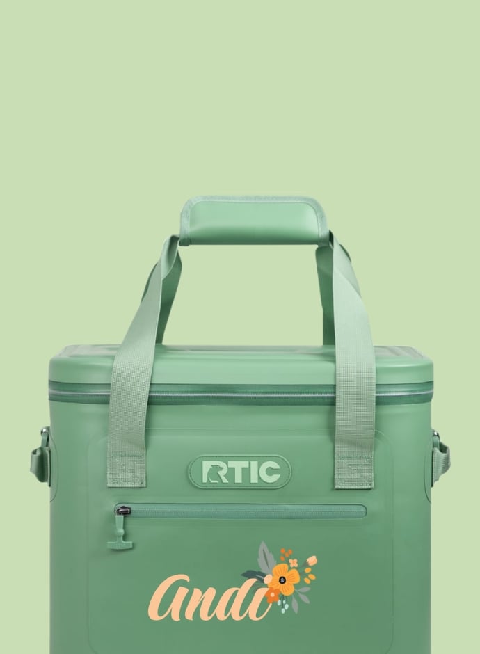 A light green RTIC soft cooler with the name Andi printed on it in yellow and a flower next to the name - on a light green background.